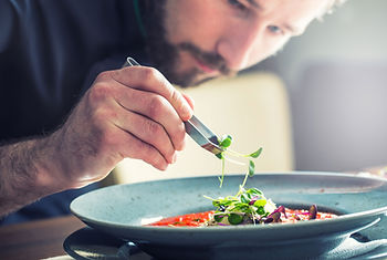 Un cuisinier qui dispose les ingrédients dans l'assiette avec une pince à épiler